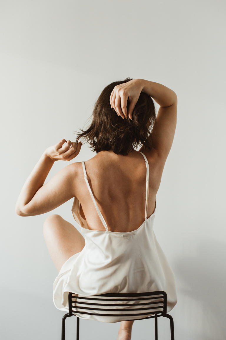 Woman in Nightgown Sitting on a Chair Facing a White Wall